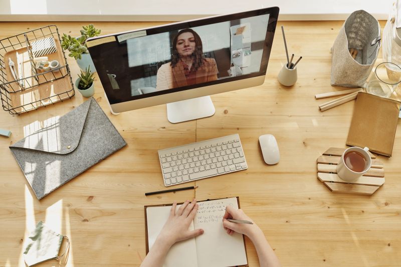 Persona con auriculares frente a una laptop durante una videollamada en una mesa de madera